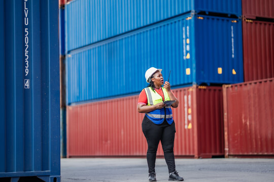 Logistics professional holding a tablet and walkie talkie in an industrial container yard, ensuring efficient cargo handling, warehouse safety, and real-time coordination in global supply chains. - Powered by Adobe