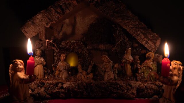 Eine Weihnachtskrippe mit zwei Engelsfiguren mit brennenden Kerzen im Vordergrund und flackerndem Licht im Fenster