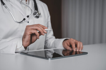 Doctor using digital tablet with stylus pen on desk in clinical setting, representing modern healthcare and telemedicine technology concept.