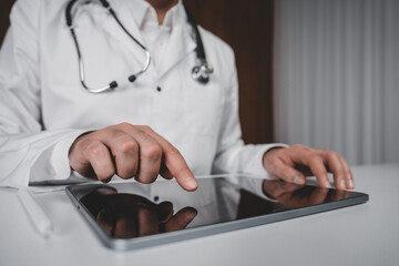 Male doctor using digital tablet during online healthcare consultation on white table in clinical setting, concept of future medical technology system.