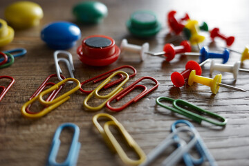 Stationery items on a wooden table with paper clips, push pins, and buttons scattered around during daylight