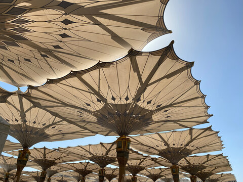 Low-angle view of the majestic retractable umbrellas providing shade in the courtyard of Al Masjid an Nabawi in Medina. The umbrellas feature intricate geometric patterns and golden columns.