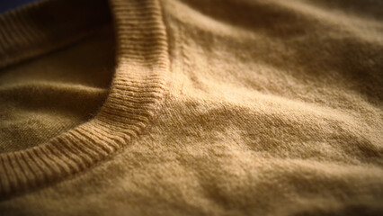 Warm-toned close-up of soft yellow woolen sweater with fuzzy texture and ribbed collar. Pullover made of natural fabric