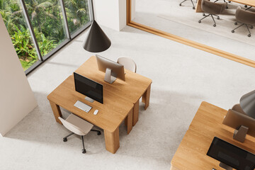 Top view of modern office interior with wooden desks, computers, and chairs near large window...