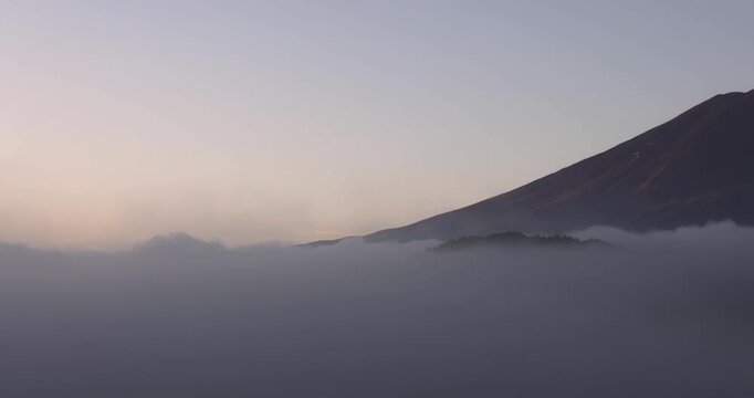 Early morning panorama of Mount Fuji rising from thick mist as the camera sweeps right, revealing gentle dawn tones on the peak above the subdued foggy foothills