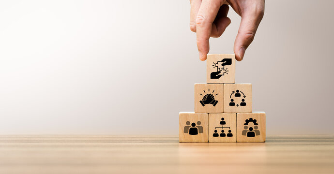 Wooden blocks arranged in a pyramid with icons representing teamwork, collaboration, leadership, organizational structure, and partnership, symbolizing corporate unity and strategic team management