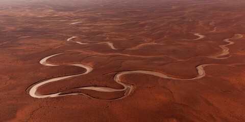 Aerial view of a winding river flowing through a desert landscape with reddish hues