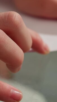 Child delicately grips paper close to glass, Child gently pinches and presses paper near glass surface, Young child carefully manipulates paper by pinching and pressing near glass surface