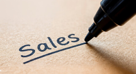 close-up of a marker pen writing the word &ldquo;sales&rdquo; on a piece of cardboard, selective focus