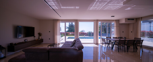  Modern open-plan living and dining room in a luxury villa with large glass doors opening to a...