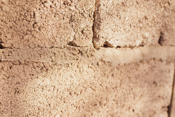 Textured wall of rectangular stone blocks in light beige shades and cement between them.