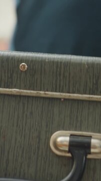 caucasian man holding green suitcase closeup with focus on rough hands gripping worn corner of case metal rivets and leather patches visible, steady lift and careful motion, interior backdrop, scuff