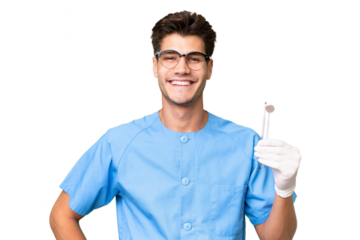 Young dentist man holding tools over isolated background posing with arms at hip and smiling