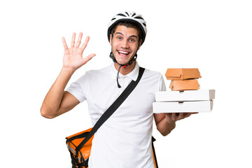 Young caucasian man with thermal backpack over isolated background saluting with hand with happy expression