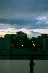 Rainy city view through window glass at dusk
