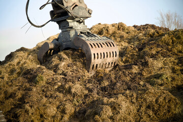 Excavator digging into a large pile of green waste during the composting and bokashi process. The machinery processes organic residual streams to produce peat-free substrate for sustainable horticultu