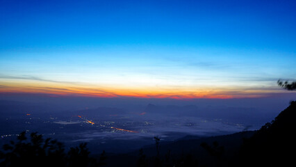 Scenic view of sunrise over high mountain, lined with pine trees, with people to watch the sunrise. Tourists travel to see the mist and the sunrise at Phu Kradueng National Park. Travel Thailand 