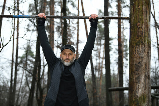 Man training outdoors with pull-up bar in forest during a cloudy day