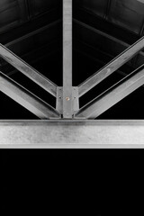 Interior metal structure with cross-shaped black steel beams and mesh panels illuminated by spotlights