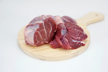 three pieces of raw beef shank on a round wooden cutting board, isolated on white background