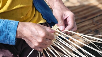 Hands weaving natural materials. Crafting bamboo basket. Basketry, basketwork or wickerwork.