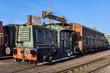 Historical green diesel shunting locomotive connected to a rusty brown cargo wagon stationed at the Veluwsche Stoomtrein Maatschappij museum.