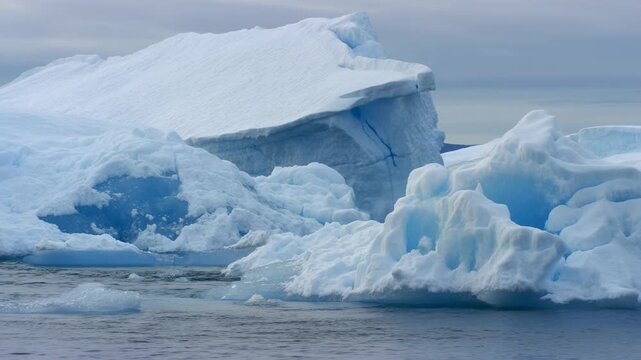 Vast icebergs float serenely on arctic waters under a cloudy sky. the massive, textured ice structures convey the majesty and fragility of polar regions, themes of climate change and environmental bea