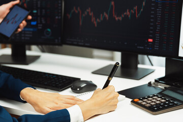 Cropped pointing hand with pen in businessman, checking with holding smartphone by woman investor online website program application with dynamic stock market at home office at back side. Infobahn.