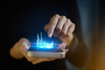 Hand holding smartphone with holographic bar chart data analysis