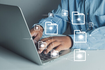Businessman using laptop with holographic folder icons, representing cloud computing, digital file management, online data storage, and secure information transfer network.