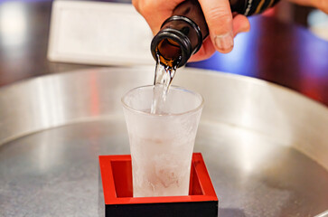 日本酒を升の中の冷えたガラスのコップに注ぐ手元のクローズアップ