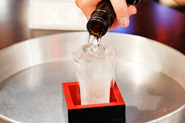 日本酒を升の中の冷えたガラスのコップに注ぐ手元のクローズアップ