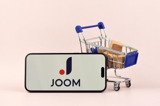 The shopping cart with a smartphone there is Joom open on the screen on white background.