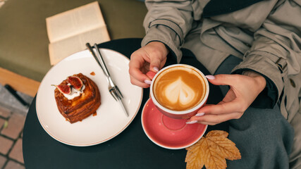 Woman holding a latte with heart art and fig pastry on a table