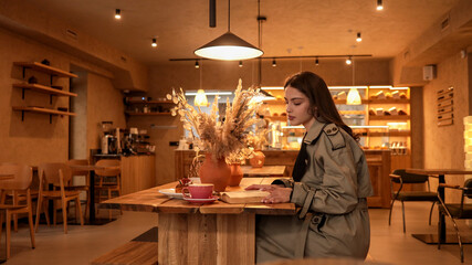 Young woman reading a book at a wooden table in a cozy cafe with a cup of coffee