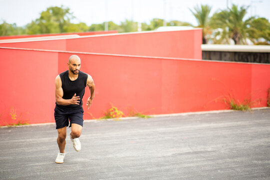 Focused young man sprinting outdoors in urban setting wearing black active wear - Powered by Adobe