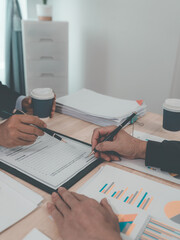 A male lawyer is working in his office, signing a contract with a male client who is seated in his...