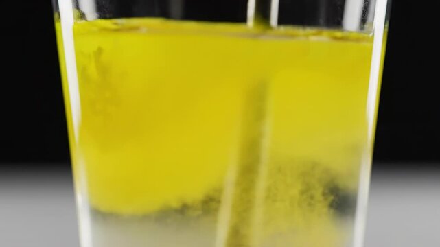 Dramatic slow motion stirring of glowing yellow supplement powder dissolving rapidly into a swirling, crystal clear hydration beverage in a glass sports, energy, dissolving rapidly