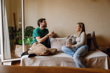 Obraz premium A woman smiles and listens to a man sitting across from her on the couch while they hold glasses