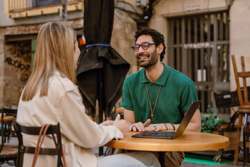 Fototapeta premium A man laughs and listens to a woman sitting across from him at a table with a laptop on it