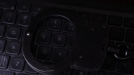 Handcuffs resting on a dark keyboard illuminated by blue light, symbolizing crime, justice, and law enforcement in a digital age with a focus on security and technology - Powered by Adobe