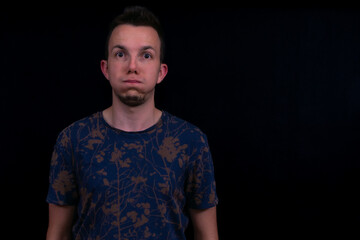 Obraz premium Funny Man Portrait With Puffed Cheeks In Blue Patterned Tshirt On Black Background