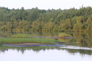 Obraz premium the banks of the Northern Cobra River, overgrown with green forest and grass, at the end of summer