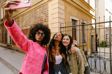 Obraz premium A woman hugs a female friend as they pose together with a female friend holding a phone while they grimace and smile