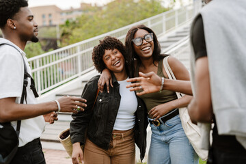 Fototapeta premium Two female friends are hugging and laughing while two male friends are next to them and one of them is talking