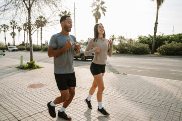 Male athlete gestures and talks to female athlete who listens and smiles while they run