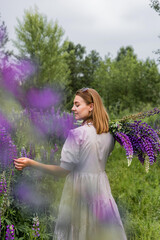 Female model in light dress among blooming lupines in summer