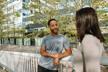 Naklejka premium A male athlete leans on the railing and smiles while listening to a female athlete standing next to him on a bridge