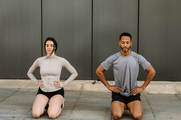 Female and male athletes holding hands on waist while kneeling on ground with eyes closed