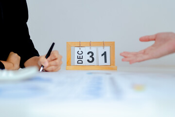 Business meeting with wooden desk calendar showing December 31, end of year deadline concept, planning, contract review, year end summary and corporate decision making.